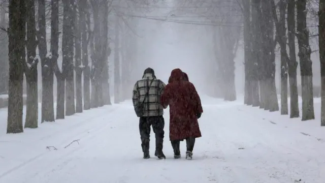 57-річний чоловік і дружина Коля та Оля йдуть крізь снігову бурю під звуки артилерійських стрілянь 12 лютого 2023 року в Часовому Яру, Україна