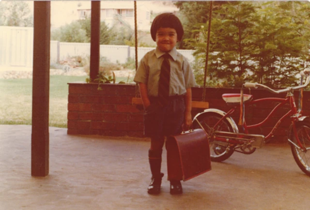 Terence Tao vestido con el uniforme escolar y un maletín sonríe a la cámara