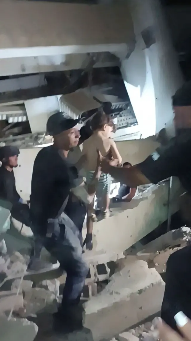 Rescatistas se pasan a un niño pequeño tras ser rescatado de entre los escombros de un edificio, después de que terremotos azotaran el país, en La Guaira.
