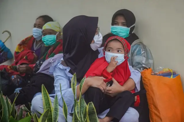 Seorang ibu menggendong anaknya dengan menggunakan masker di pos pengungsian.
