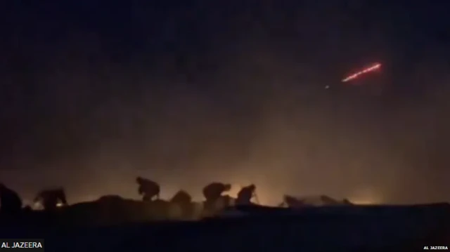 আল জাজিরার এই ছবিতে রেড ট্রেসার ছুটে আসতে এবং মানুষদের বহরের পেছনে গাড়ির আড়ালে আশ্রয় নিতে দেখা যাচ্ছে