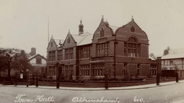 Fotografía de época en blanco y negro del Ayuntamiento de Altrincham, procedente del archivo del Ayuntamiento de Trafford. El edificio de ladrillo se alza en la esquina de una calle.