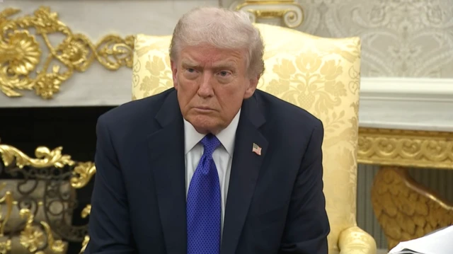 ډونلډ ټرمپ په شینبخونه درېشۍ کې ناست دی، شنه نېکټايي یې اچولې او سپين کمیس یې په تن دی.