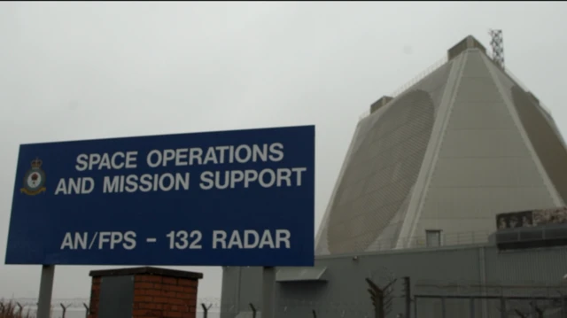 تابلوی بیرون پایگاه نیروی هوایی سلطنتی فیلینگدِیلز، پشت تابلوی آبی رنگ، بنای بتونی بزرگ دیده می‌شود