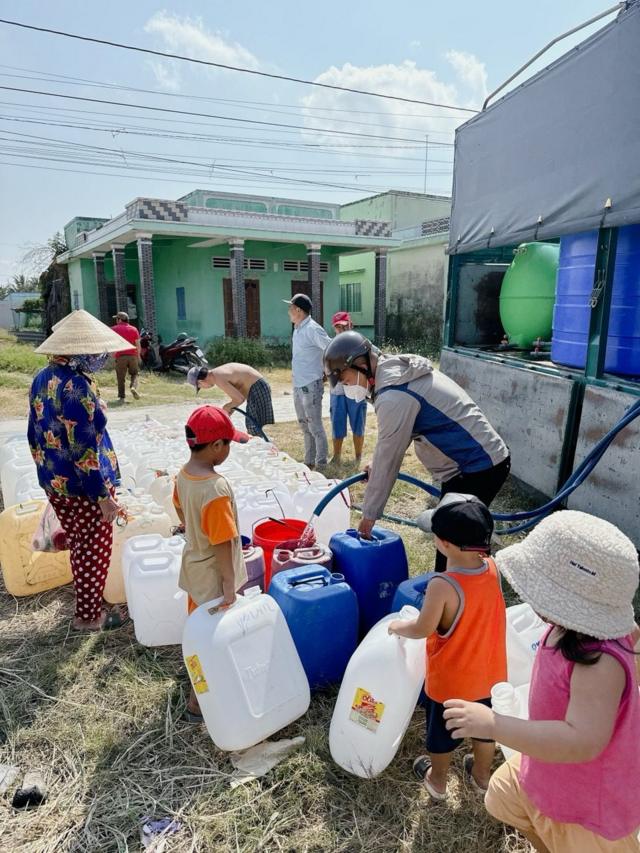 Trẻ em cùng người thân dùng can nhựa đi lấy nước tại ấp 3 Rạch Già, huyện Gò Công Đông, tỉnh Tiền Giang từ xe nước của các mạnh thường quân vào ngày 9/4