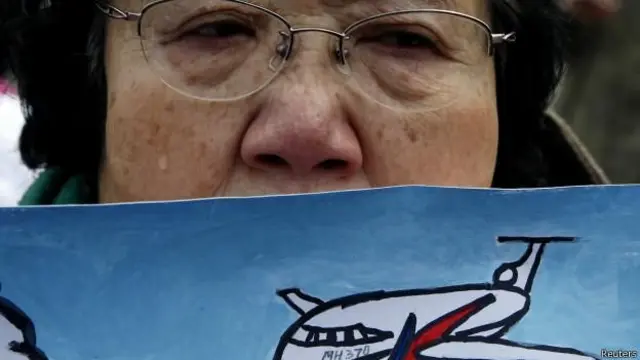 Mulher idosa chorando segurando um desenho representando o voo MH370