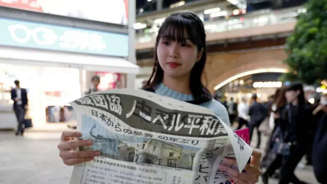 日本被団協のノーベル平和賞受賞を伝える新聞号外を読む女性（11日夜、東京）