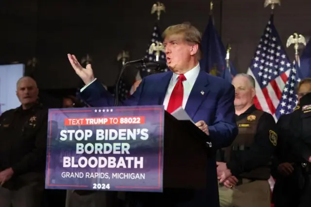 Trump discursando; abaixo dele, cartaz com slogan 'Vamos parar com o banhoqual a melhor casa de apostas hojesanguequal a melhor casa de apostas hojeBiden na fronteira'