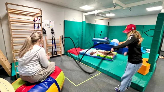 Dos alumnos en la sala de terapia ocupacional. Uno está sentado en un inflable mientras el otro sostiene cuerdas.