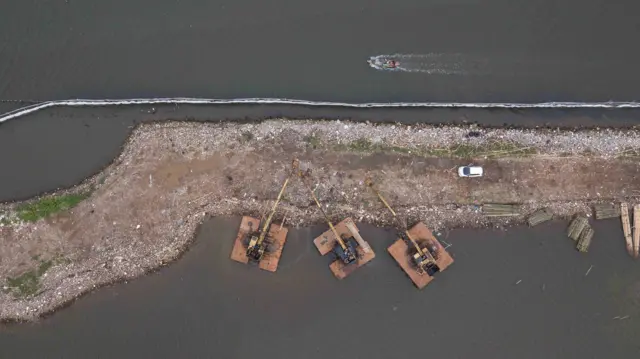 Foto udara alat berat terparkir di samping pagar laut yang terpasang di kawasan pesisir Tarumajaya, Kabupaten Bekasi, Jawa Barat, Selasa (14/1/2025). Menurut nelayan setempat pemasangan pagar laut yang membentang sepanjang 2 km itu mengganggu lalu lintas kapal kecil dan berpotensi merusak ekosistem laut karena adanya pengerukan tanah. 
