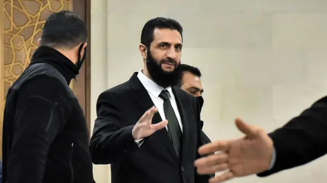 أحمد الشرع، مرتديًا حُلة، يلوح للمصورين في دمشق