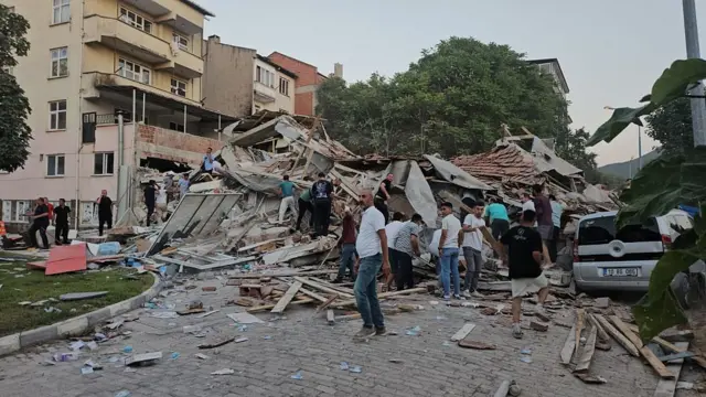 Sındırgı depreminde yıkılan bir binanın etrafında toplanmış insanlar