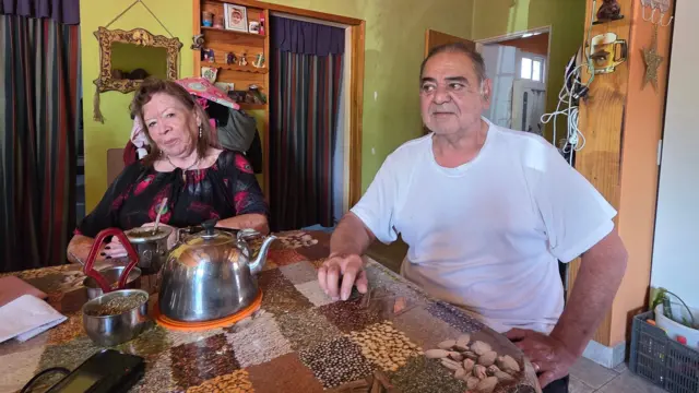 Una mujer y un hombre sentados a la mesa tomando mate