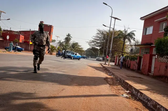 Un homme en tenue militaire marche sur une rue à Bissau