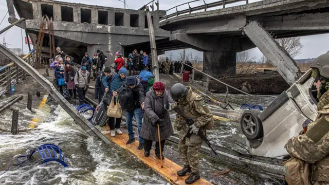 Pipo cross di river through one makeshift bridge as dem dey flee di frontline town of Irpin, near Kyiv, Ukraine - 7 March 2022.