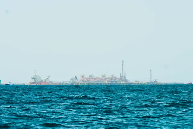 Une plateforme gazière en mer est visible à l'horizon, avec l'océan devant elle et un large panorama du ciel au-dessus.