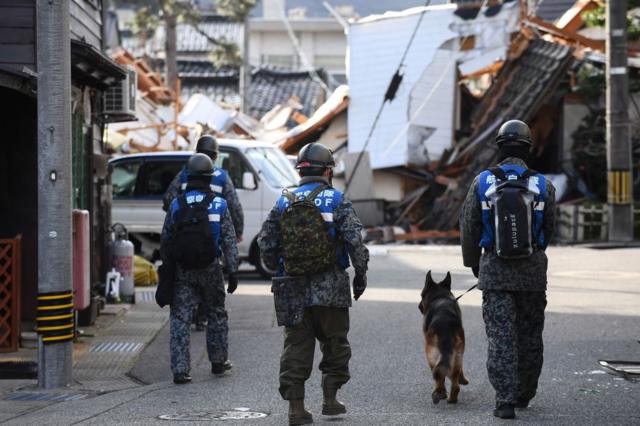Pasukan Bela Diri Jepang berjalan dengan seekor anjing untuk mencari korban gempa di kota Wajima, Prefektur Ishikawa, pada Jumat, 5 Januari 2024.