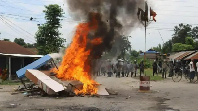 देवानगन्जमा दुई समुदायबीच तनाव फैलिएपछि सडकमा जलाइएका सामानहरू, पछाडि सुरक्षाकर्मीहरू देखिन्छन्
