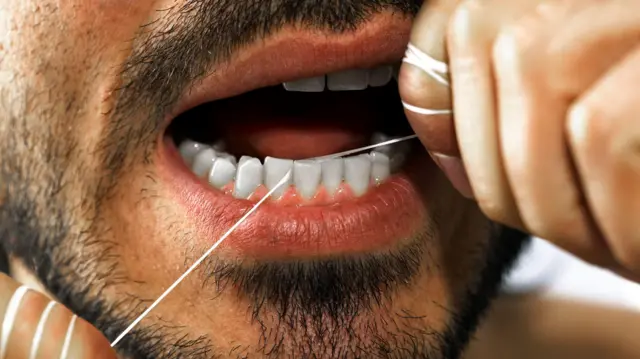 Imagem da boca e do rosto de um homem passando fio dental entre os incisivos