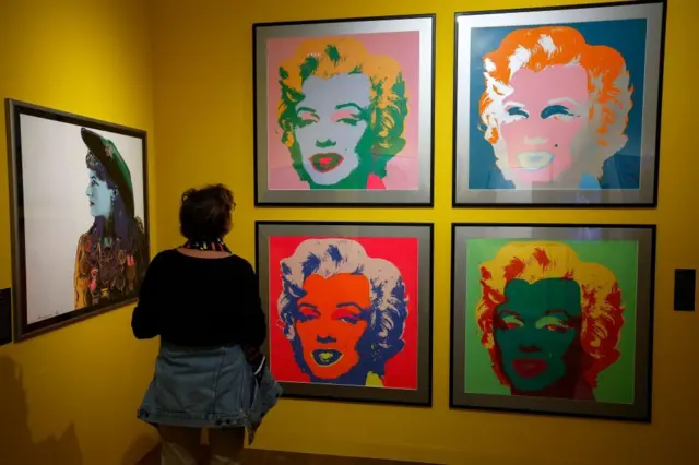 Женщина на выставке разглядывает принты Энди Уорхола с портретом Мэрилин Монро