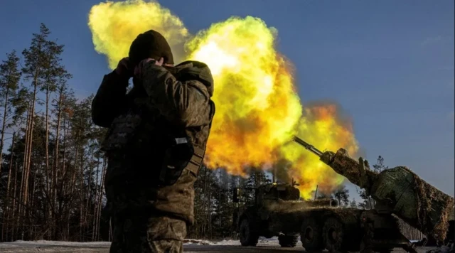 Un soldat pose à côté de véhicules de combat