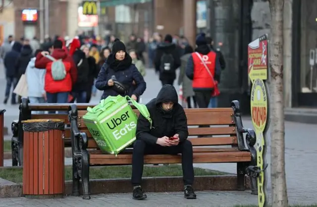 Юнак із великою зеленою торбою Uber Eats сидить на лавці на Хрещатику, Київ