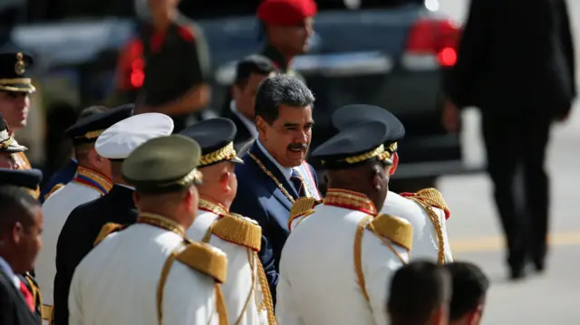 Maduro, um homem branco,jogos de apostas a partir de 1 realcabelos grisalhos e bigode, está no meiojogos de apostas a partir de 1 realvários homens vestidos com uma roupa formal branca e boina