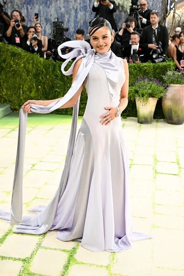 Chase Sui Wonders wear lavender gown wit panels in alternating fabrics. She hold long piece of fabric from her neck bow for her right hand.