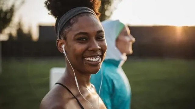 سيدتان تبتسمان أثناء ممارسة الرياضة إحداهما محجبة والثانية تضع سماعة أذن