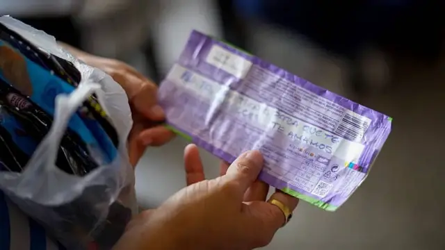 La esposa de Ángel Godoy, Adriana Briceño, sostiene un envoltorio con un mensaje escrito en tinta azul que dice "Papito, aquí tienes para que te endulces. Te amamos".