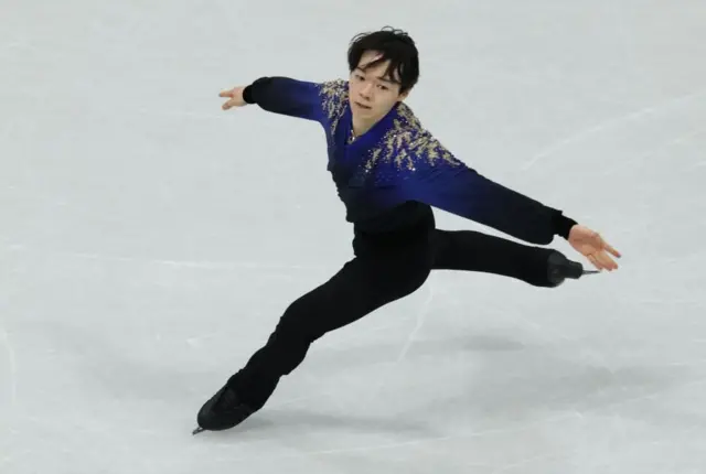 肩の部分が青く、それ以外は黒い衣装の鍵山が、両手を広げ、左足だけ氷につけて滑っている