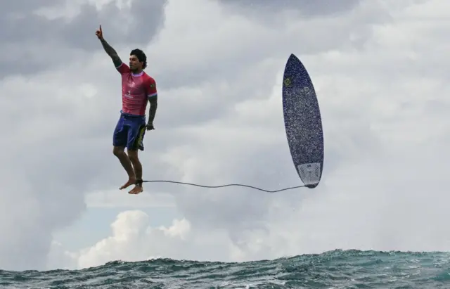 O surfista Gabriel Medina parece estar suspenso no ar sobre o mar, ao ladonetbet logosua prancha, que também parece suspensa