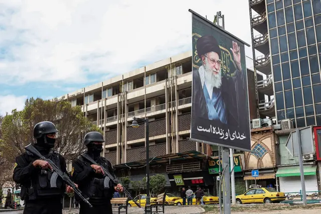 Miembros de las fuerzas de seguridad iraníes hacen guardia este lunes en una calle junto a una valla publicitaria del líder supremo de Irán, el ayatolá Ali Khamenei, fallecido en los primeros ataques del sábado.