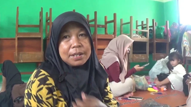 Anik Hatamah, pengungsi erupsi gunung semeru menggunakan jilbab hitam berada di ruang kelas yang menjadi posko pengungsi.