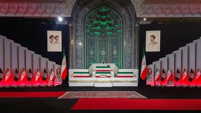 توابيت مغطاة بأعلام إيرانية في باحة مسجد بساط أحمر وأعلام إيران ورايات إسلامية - التابوت الأول من الأعلى فوقه عمامة سوداء في إشارة إلى جثمان علي خامنئي