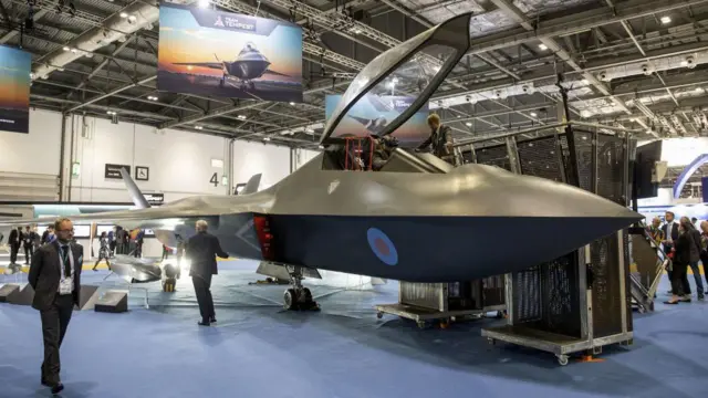 جت جنگی در فضای سرپوشیده نمایشگاه و شرکت‌کنندگان در کنارش