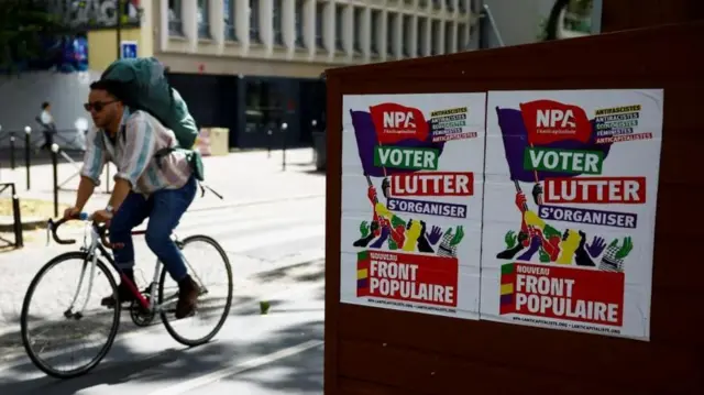 Una persona pasa en bicicleta al lado de carteles del NFP