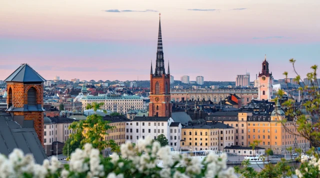 Na panoramę Sztokholmu składają się ceglane kościelne wieże, kamienice o białych i żółtych fasadach i widoczne na dalszym planie bloki mieszkalne.