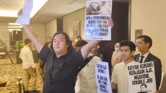 Andrie Yunus sedang membentangkan poster menolak pembahasan rapat revisi UU TNI dalam ruang tertutup.