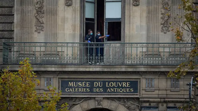 Dos policías usando tapabocas se asoman por una puerta en el segundo piso de Museo del Louvre y señalan hacia la derecha.