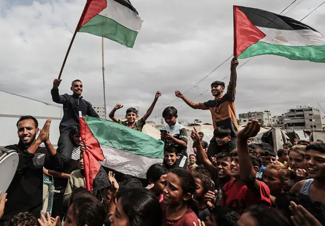 مجموعة من الفلسطينيين بأعمار مختلفة يحملون العلم الفلسطيني محتفلين. الصورة التقطت نهاراً وتظهر السماء ملبدة بالغيوم.