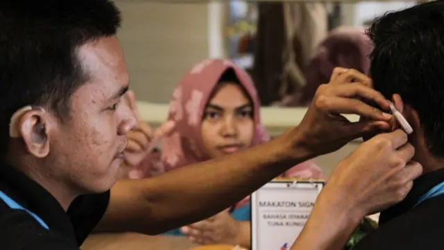Seorang tunarungu membantu memasangkan alat bantu dengar kepada temannya.