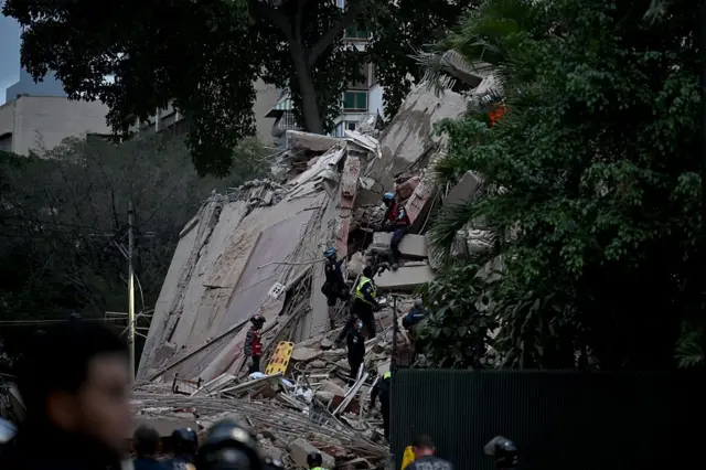 La fachada de un edificio colapsado mientras rescatistas escalan el muro en búsqueda de víctimas