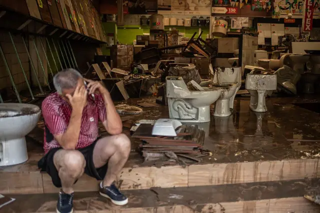 Un hombre habla por teléfono sentado en una tienda de materiales de construcción afectado por las inundaciones