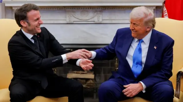 Macron e Trump sentados, sorrindo e apertando as mãos