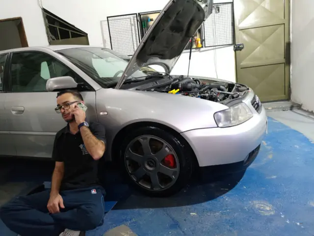 Osmar sentado ao lado do carro com motor aberto enquanto fala ao celular