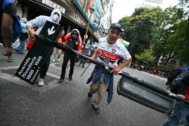 Torcedor segurando poste com placa de rua durante protesto em Buenos Aires