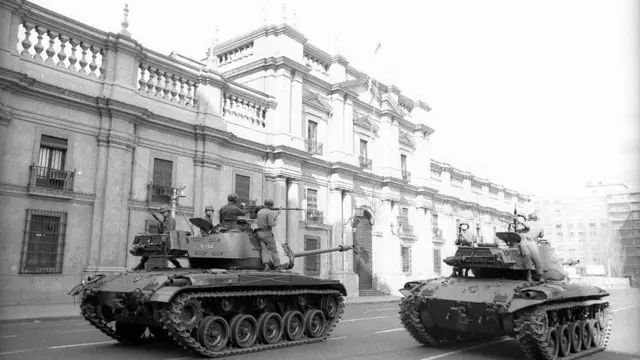 Photo d'archive de 1973 : À 10 heures, des chars militaires sont arrivés devant La Moneda et les tirs se sont poursuivis à la suite du coup d'État mené par le commandant de l'armée, le général Augusto Pinochet. La photo en noir et blanc montre deux chars militaires s'approchant d'un grand bâtiment administratif, avec des soldats pointant leurs fusils et prêts à tirer.