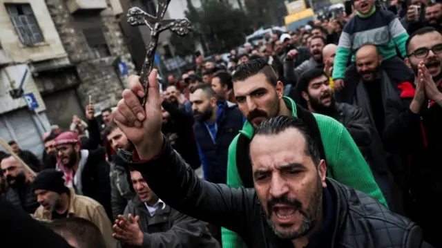 Imagembetesporte tela inicialuma multidãobetesporte tela inicialmanifestantes marchando por uma rua. Em primeiro plano, um homem barbudo segura uma pequena cruz enquanto grita