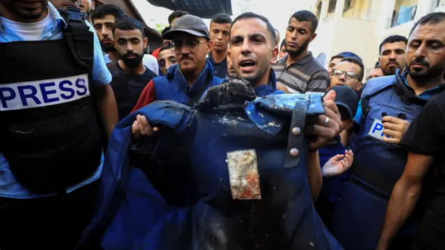 انس شریف در مراسم تشییع همکارش اسماعیل الغول، خبرنگار الجزیره که ژوئیه ۲۰۲۴ در حمله هوایی اسرائیل کشته شد، جلیقه ضدگلوله او را در دست دارد
